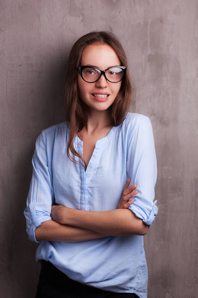 portrait of beautiful happy young woman wearing glasses near grey grunge wall - 写真・画像