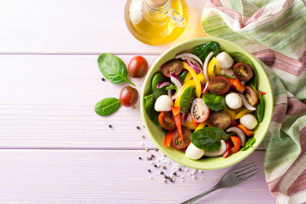 Fresh salad with spinach, bell peppers, tomatoes, red onions and mozzarella on purple wooden background. - Foto, immagini