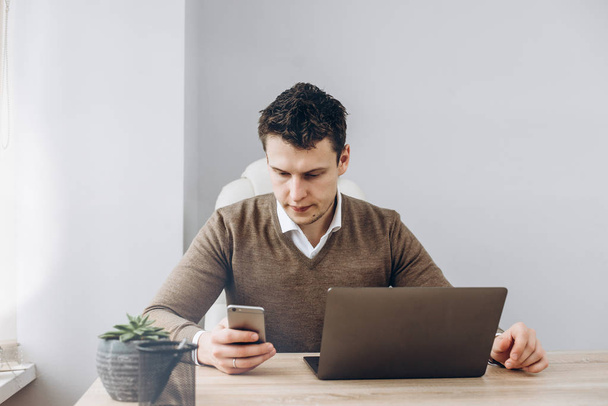 Jeune homme d'affaires travaille sur ordinateur portable dans son bureau, et à la recherche d'informations dans son smartphone
 - Photo, image