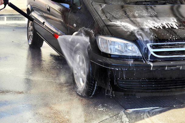 Καθαρισμός αυτοκινήτου χρησιμοποιώντας υψηλής πίεσης νερού. Ο άνθρωπος πλύσιμο του αυτοκινήτου υπό υψηλή πίεση νερού στην υπηρεσία  - Φωτογραφία, εικόνα