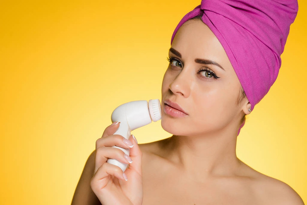 cute young girl with a pink towel on her head doing a deep cleansing of the skin of the face with an electric brush - Photo, image