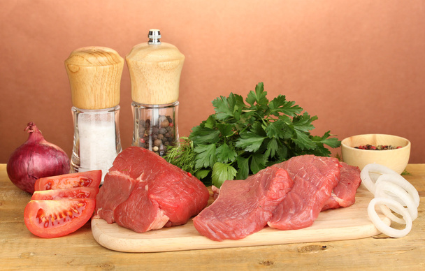 Raw beef meat with spices on wooden table on brown background - Photo, Image