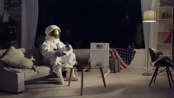 4K Astronaut relaxing in apartment, watching TV and drinking a beer - Video