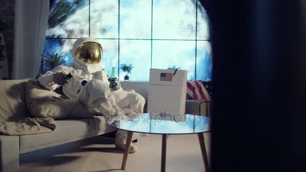 4K Astronaut relaxing in apartment, watching TV and drinking a beer - Záběry, video