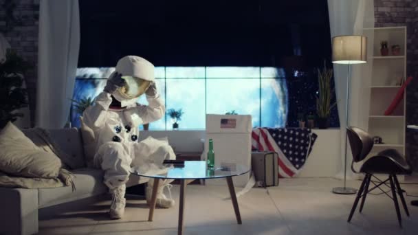 4K Astronaut taking helmet off, relaxing in apartment, watching TV and drinking a beer - Video