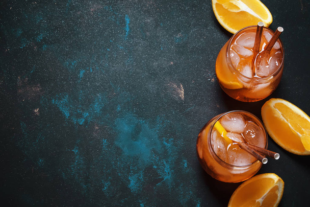 Summer alcoholic cocktail with bitter, sparkling wine, soda, orange and ice, dark background, top view - Фото, изображение
