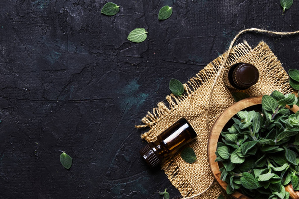 Essential oregano oil in a glass bottles and a bunch of fresh herbs, black background, top view - Fotografie, Obrázek