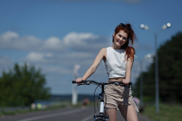 rusovlasá mladá dívka v šortkách a topy představují stojící s kol - Fotografie, Obrázek