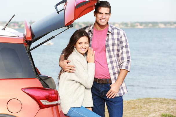 Young couple near car on river bank - Foto, imagen