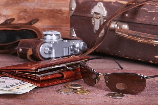 Travel concept with Vintage suitcase, sunglasses, old camera, suede boots, case for money and passport on wooden floor. - Foto, Imagem