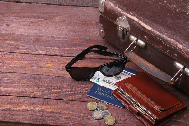 Travel concept with Vintage suitcase, sunglasses, old camera, suede boots, case for money and passport on wooden floor. - Foto, afbeelding