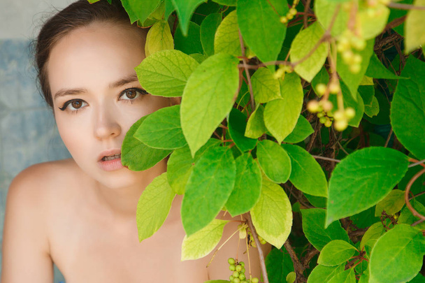 Portrait of a girl with bare shoulders covering her eyes with a leaf - Photo, Image