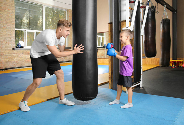 Little boy with trainer near punchbag in gym - Фото, изображение
