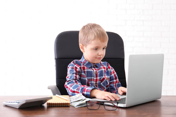 Cute little boy with laptop and money at table indoors - Photo, Image