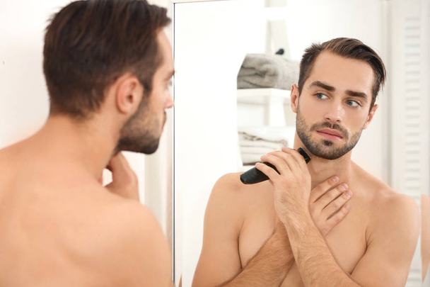 Young man shaving and looking in mirror in bathroom - Фото, зображення