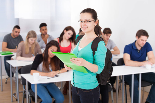 Portrait Of A Smiling Female Student Holding Folder In Classroom - Photo, Image