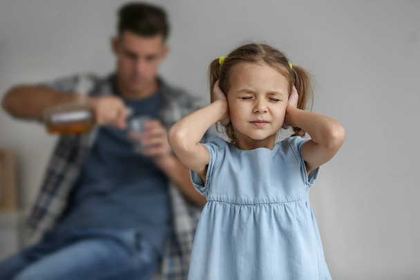 Little girl covering ears and her father drinking alcohol on background - Foto, Imagen
