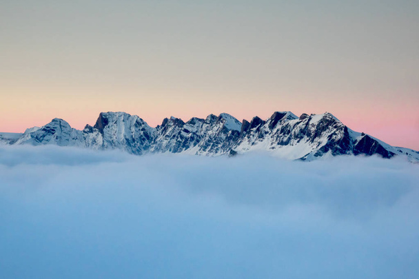 ορεινό τοπίο πάνω από πυκνά σύννεφα καλύπτουν κάτω από ένα ηλιοβασίλεμα το βράδυ ουρανό στις Άλπεις το χειμώνα - Φωτογραφία, εικόνα