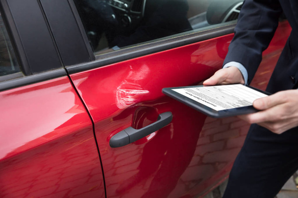 Red Car Near Person's Hand With Digital Tablet Showing Insurance Claim Form On Screen - 写真・画像