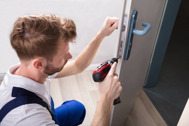 Carpintero joven instalar cerradura de puerta con destornillador inalámbrico
 - Foto, imagen