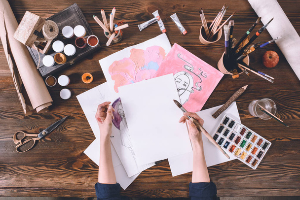 Zugeschnittene Aufnahme einer Künstlerin, die Skizzen am Arbeitsplatz mit Farben und Pinseln malte - Foto, Bild