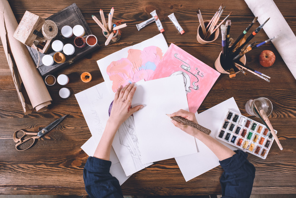 Ansicht von oben: Künstlerin malt Skizzen am Arbeitsplatz mit Farben und Pinseln - Foto, Bild