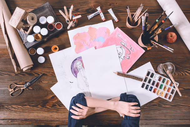 обрезанный снимок женских рук и эскизов с красками на рабочем месте художника
 - Фото, изображение