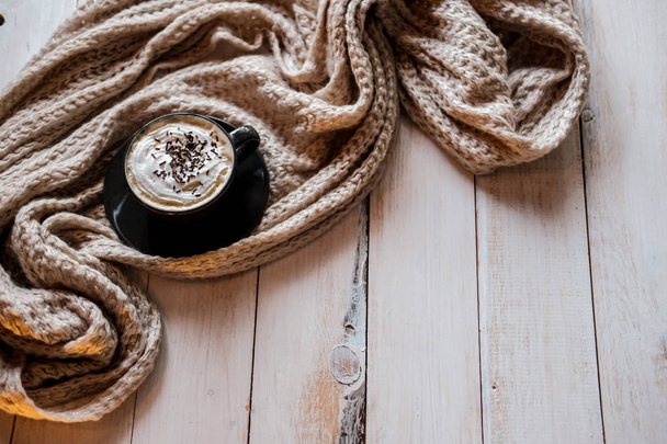 Горячий кофе на деревянном фоне и обернутый мягким шарфом.
. - Фото, изображение