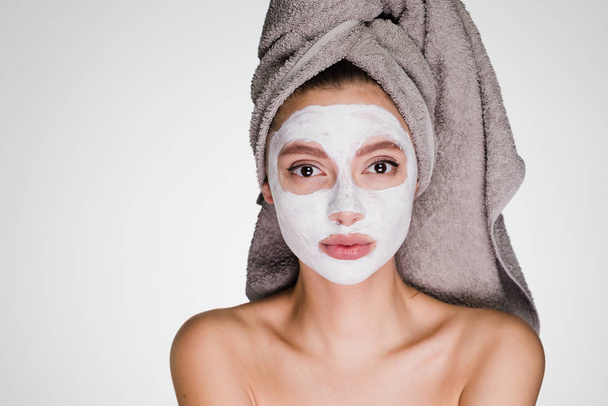 an attractive girl with a towel on her head applied a white moisturizing face mask - Valokuva, kuva