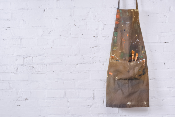 brown apron with paint brushes hanging on white brick wall   - Valokuva, kuva