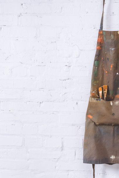 tablier marron avec pinceaux suspendus au mur de briques blanches
  - Photo, image
