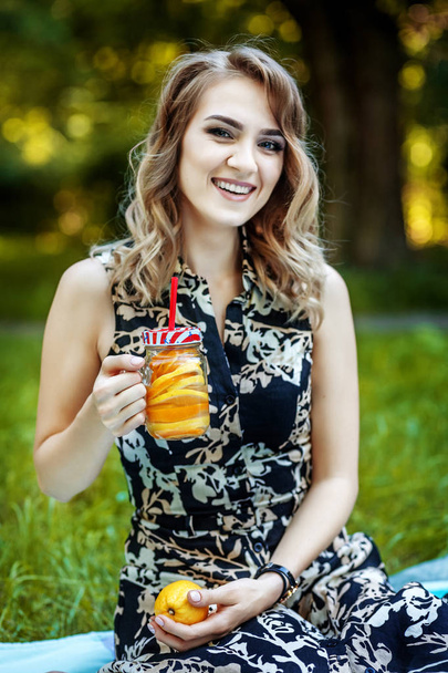 Young happy girl sitting in the park. The woman drinks detox - 写真・画像