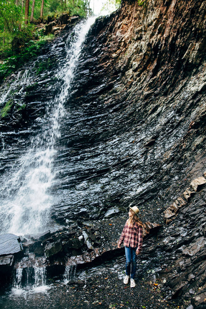 Retrato de una joven cerca de la cascada. Jovencita posa sobre el fondo del agua que cae del acantilado, cubierto de hierba, arbustos y bosque. Sesión de fotos en la ciudad salvaje fuera
 - Foto, Imagen