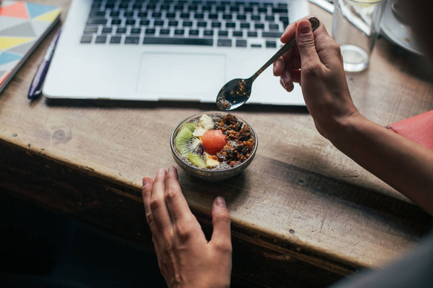 cropped view of person holding spoon near chia pudding with fruits and nuts by laptop - Fotó, kép