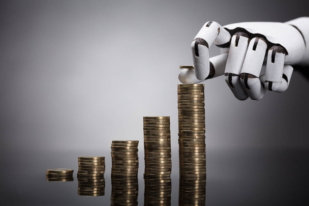 Close-up Of A Robot's Hand Stacking Golden Coins On Grey Background - Fotografie, Obrázek