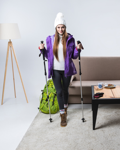 beautiful sportswoman in warm clothing with backpack and hiking sticks at home - Фото, изображение