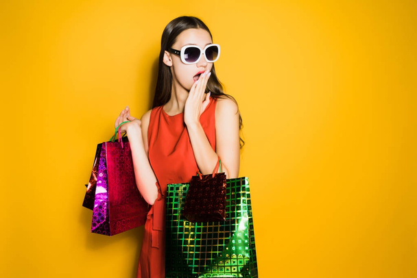 surprised young girl shopaholic in sunglasses bought a lot of gifts for the new year, surprised by discounts - Zdjęcie, obraz