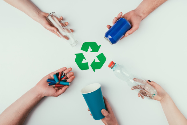 vista parcial de personas que muestran varios tipos de basura alrededor del cartel de reciclaje aislado en gris
 - Foto, Imagen