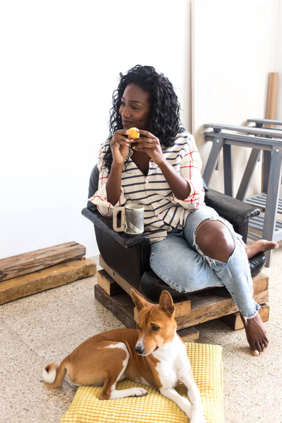 portrait of African woman with food and drink posing on chair by lying dog - Foto, imagen