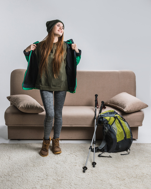 onnellinen nainen lämpimissä vaatteissa reppu ja vaellus laitteet sohvalla
 - Valokuva, kuva