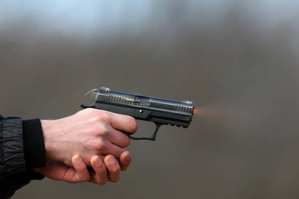 Close-up foto van een pistool schieten met twee handen, de schelpen die afkomstig zijn van de sluiter en blauw rook op een onscherpe achtergrond. - Foto, afbeelding