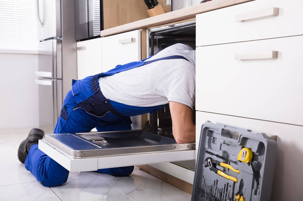 Young Male Technician Repairing Dishwasher In Kitchen - Foto, imagen