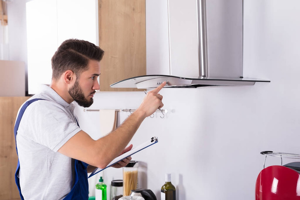 Male Electrician With Clipboard Repairing Kitchen Extractor Filter - Photo, Image