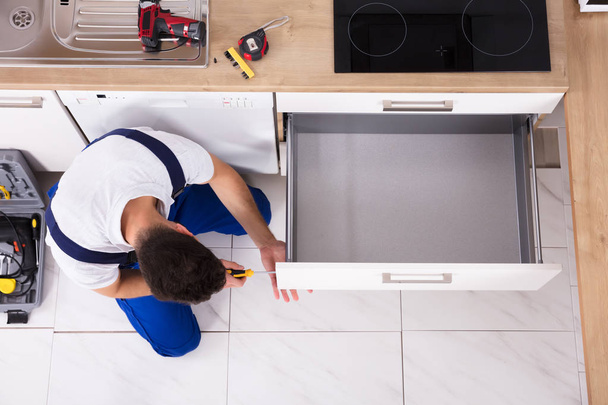 High Angle View Of Male Carpenter Fixing Drawer In Kitchen - 写真・画像