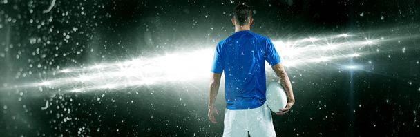 Rear view of rugby player holding ball aside against spotlights - Фото, изображение