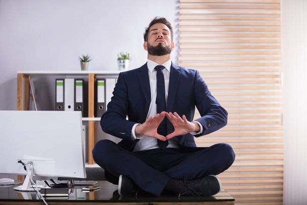Young Businessman Sitting On Desk Doing Yoga In Office - Fotoğraf, Görsel