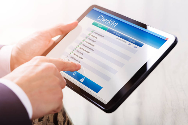 Close-up Of A Businessperson's Hand Filling Checklist Form On Digital Tablet - Foto, Imagen