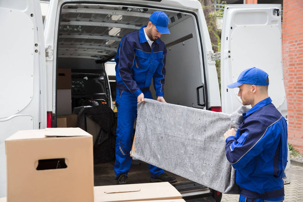 Deux jeunes travailleurs masculins en uniforme bleu déchargeant des meubles du camion
 - Photo, image