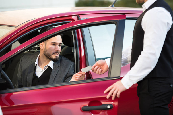 Valet Giving Receipt To Young Male Businessperson Sitting Inside Red Car - Foto, Imagen