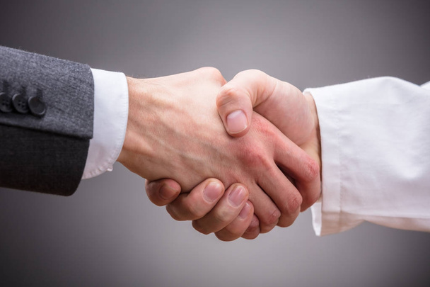 Close-up Of Doctor And Businessman Shaking Hands On Grey Background - Fotografie, Obrázek